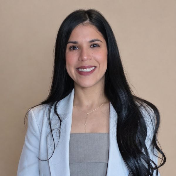 Smiling woman with long dark hair wearing a light gray blazer and beige background professional portrait pose Smiling woman with long dark hair wearing a light gray blazer and beige background; professional portrait pose.